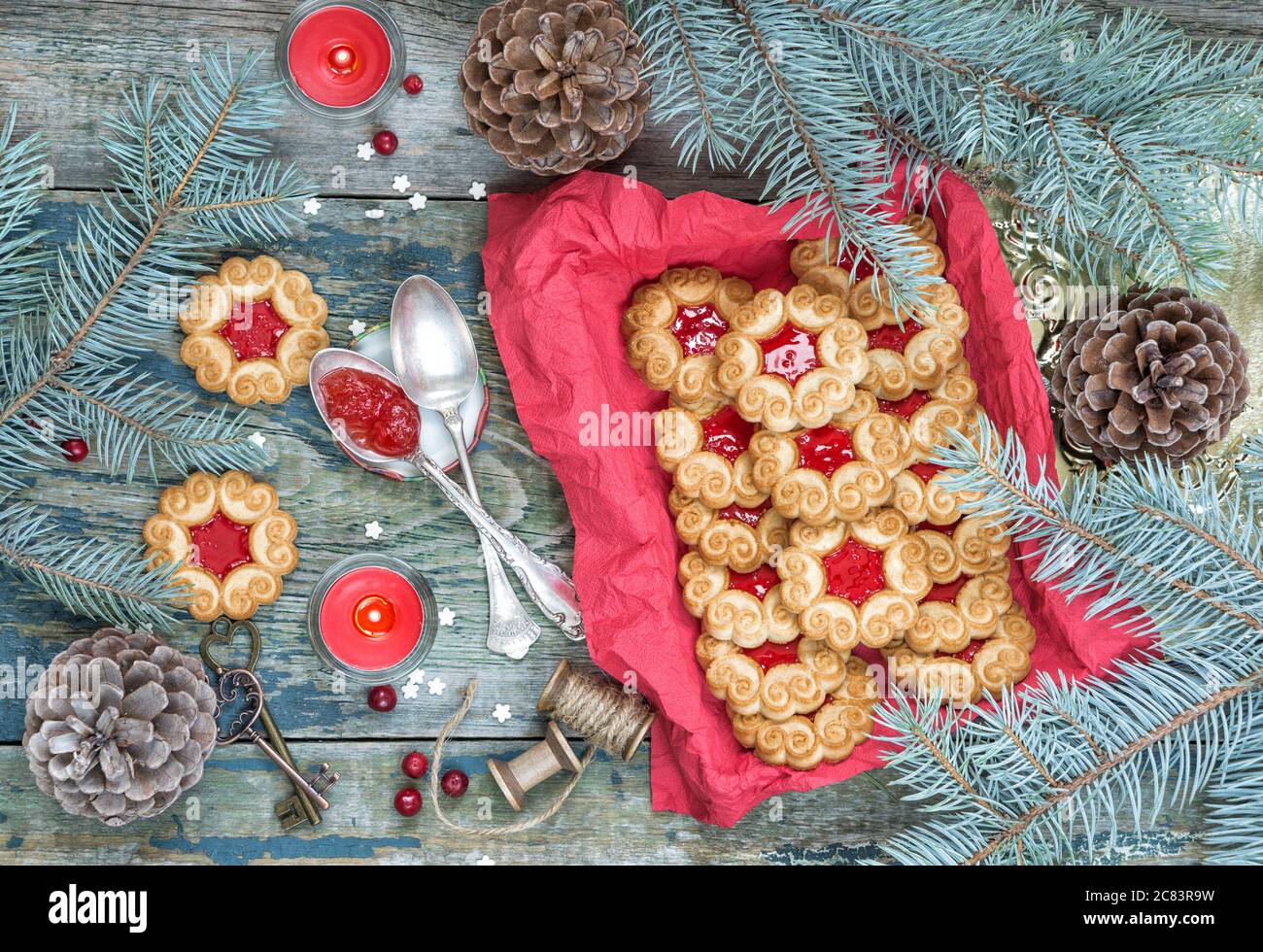 Christmas composition with sweet cookies with jam, fir branches and cones  and the burning red candle on the old wooden table, top view Stock Photo
