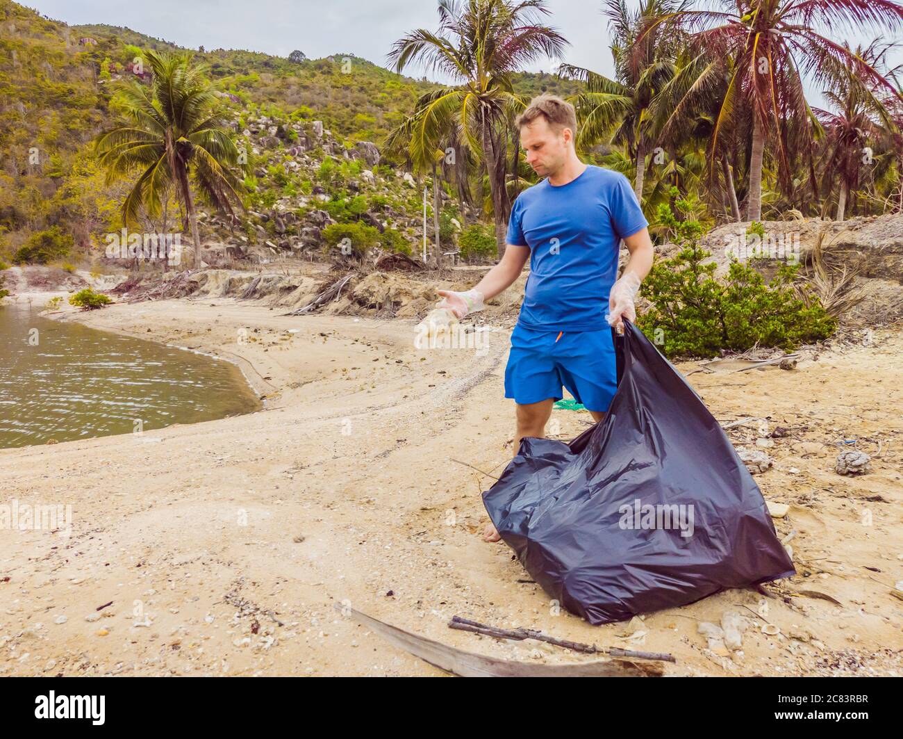 Man in gloves pick up plastic bags that pollute sea. Problem of spilled