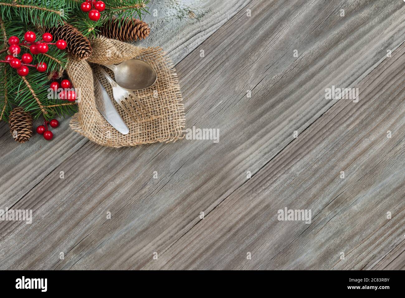 Christmas table with Christmas decoration: old knife, spoon and fork lie on the sacking napkin, as well as red holly berries and green spruce branch, Stock Photo