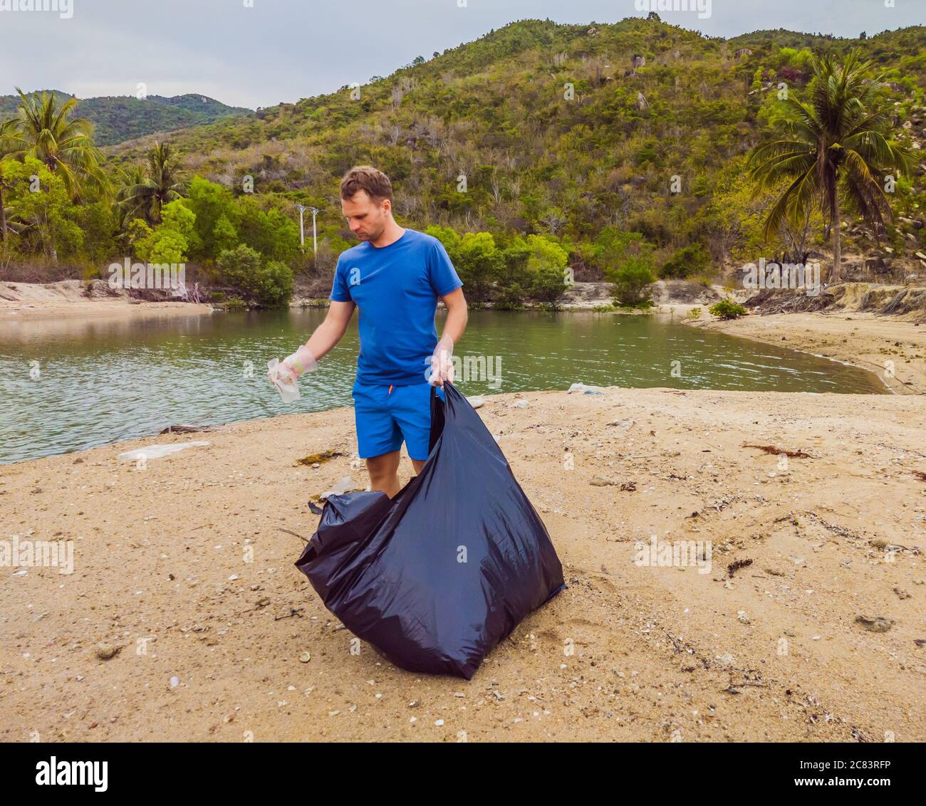 Man in gloves pick up plastic bags that pollute sea. Problem of spilled