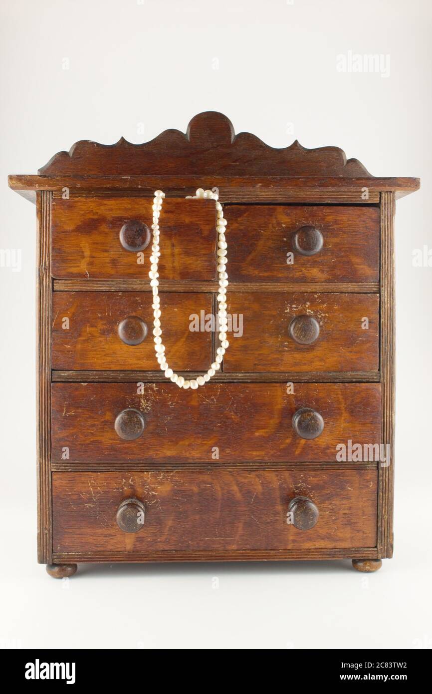 miniature chest of drawers with natural pearl necklace hanging out of one of the draws, isolated on white Stock Photo