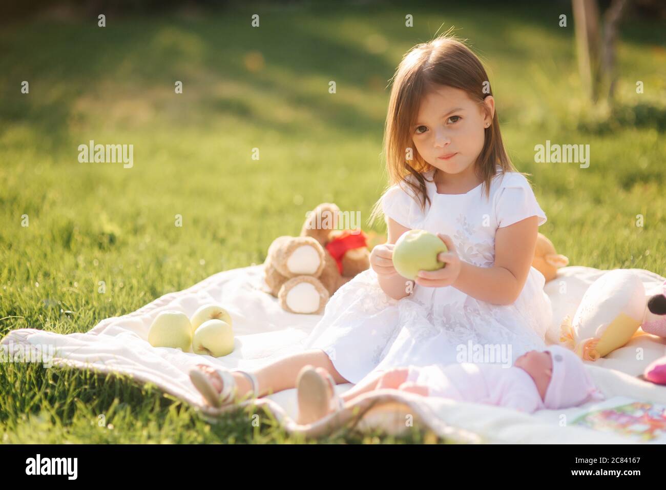 Adorable little girl sits on plaid outdoors and eat apple. Happy smiled ...