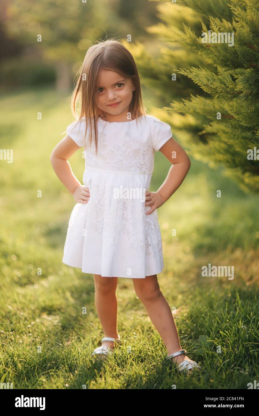 Beautiful little girl in white dress walking outdoors on back yaer of ...