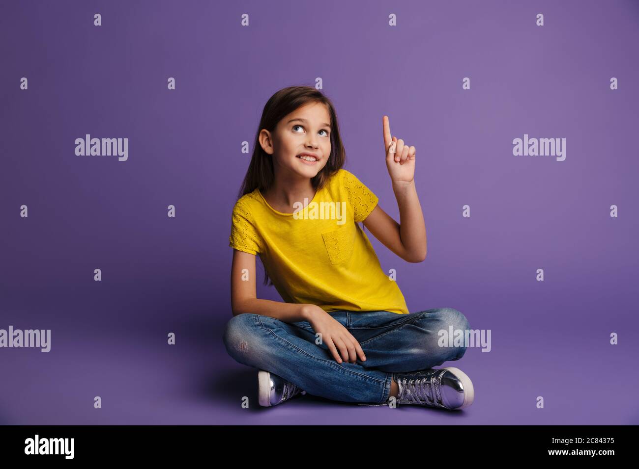 Photo of smiling cute girl pointing finger upward while sitting on ...