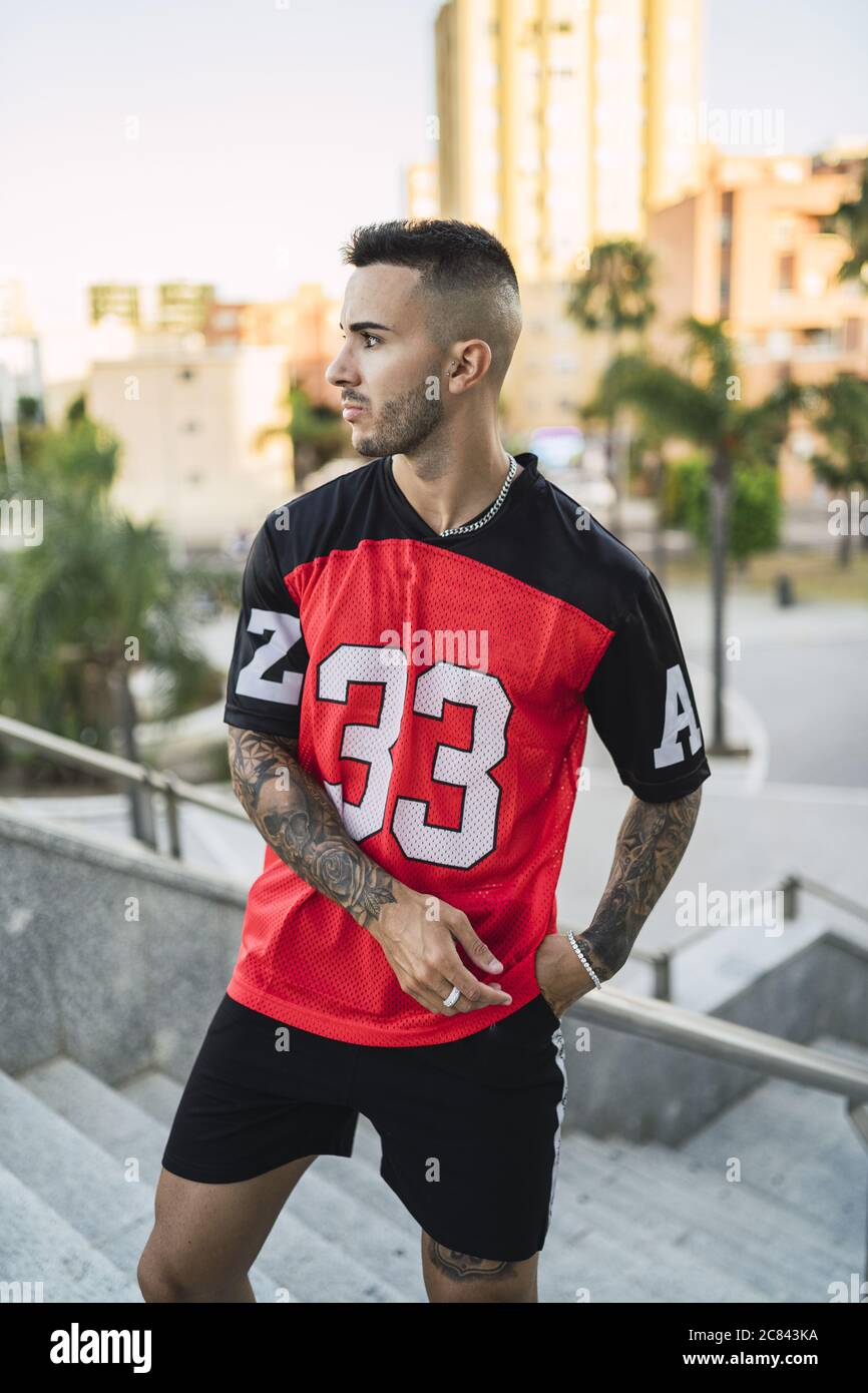 European hip male in a sporty outfit with red and black shorts and shirt,  tattoos, and metal chain Stock Photo - Alamy