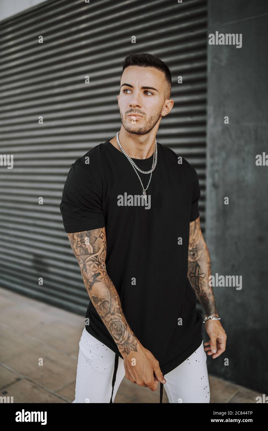 European tattooed hip male in a black shirt and white ripped jeans, and  metal chain Stock Photo - Alamy