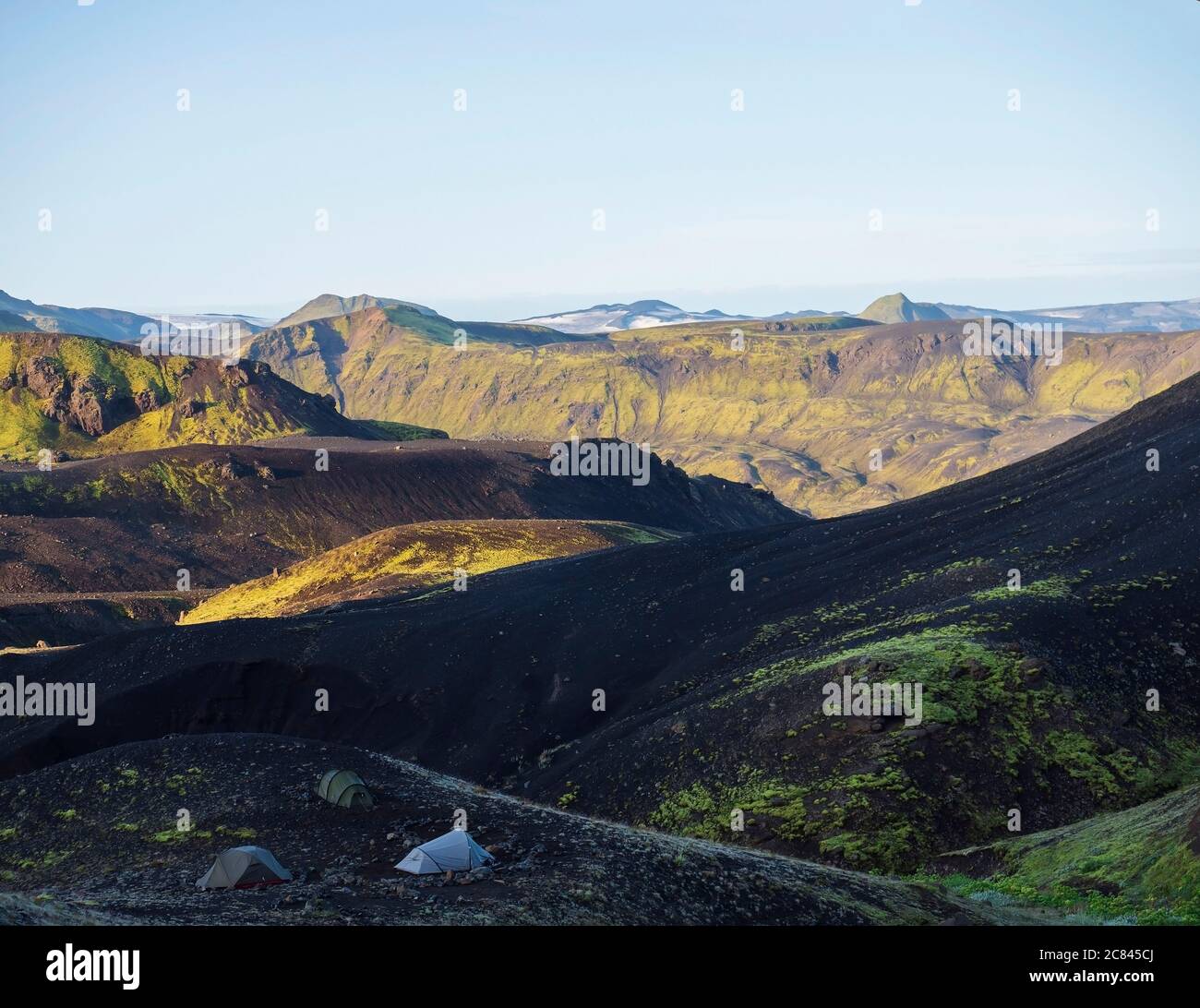Three tents alone in Botnar campsite at Iceland on Laugavegur hiking trail, green valley in volcanic landscape among lava fields with view on Stock Photo