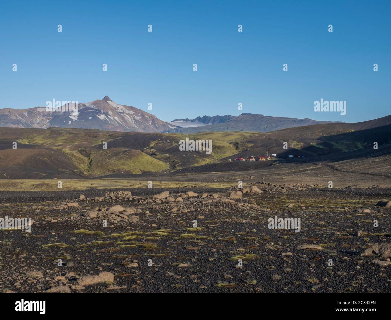View on mountain hut at Iceland on Laugavegur hiking trail, green valley in volcanic landscape among lava fields. Early morning, summer blue sky Stock Photo