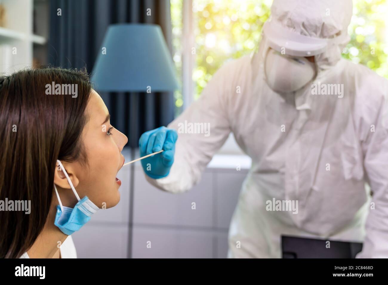 Medical staff with PPE suit test coronavirus covid-19 to asian woman by throat swab at home. New normal healthcare service at home and medical deliver Stock Photo