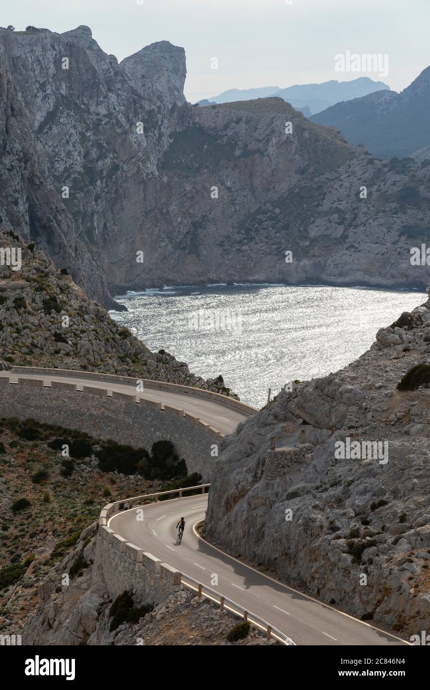 A lone cyclist descends a road on Cap de Formentor with dramatic cliffs in background, Mallorca Stock Photo