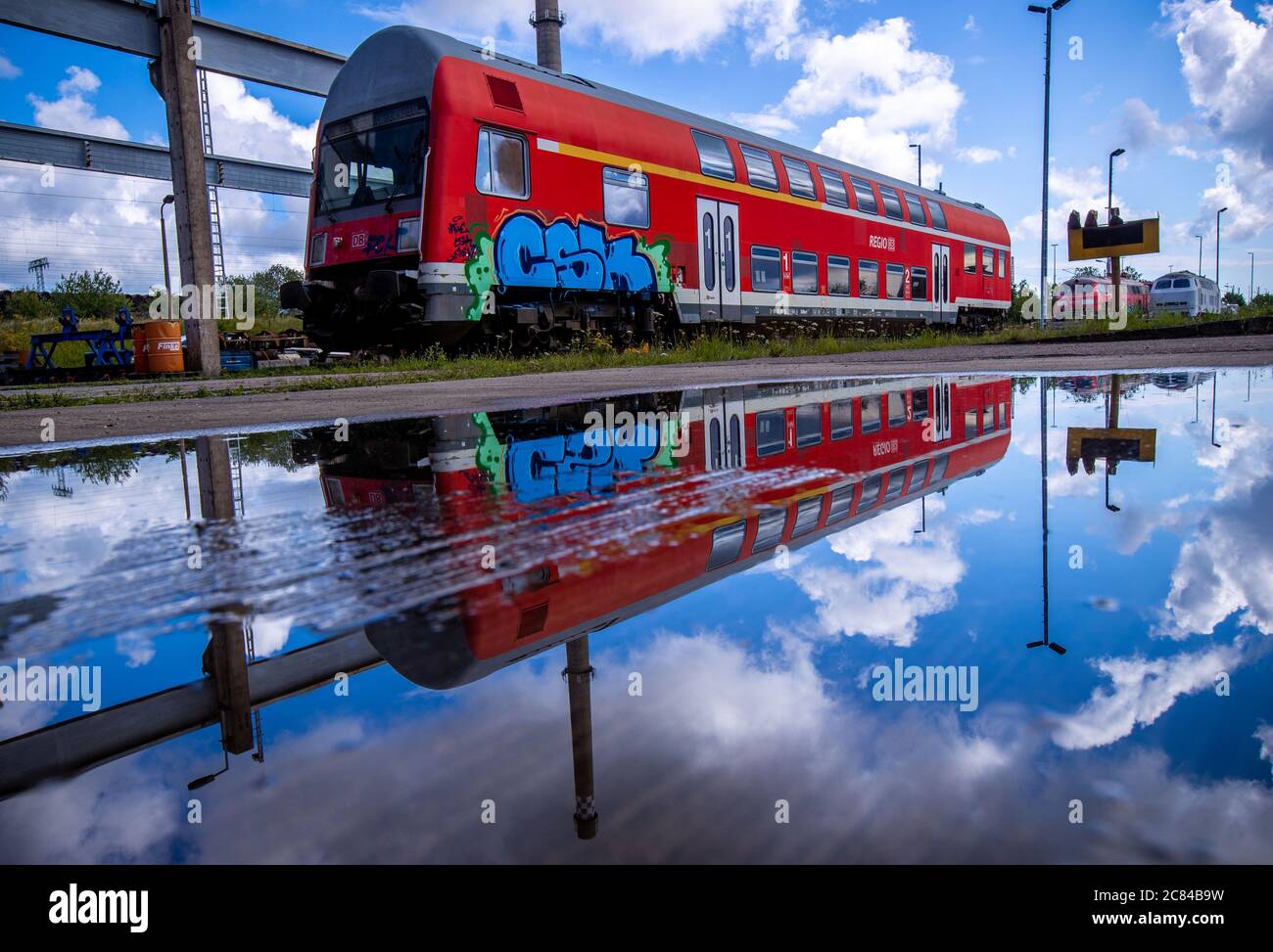 16 July 2020, Mecklenburg-Western Pomerania, Mukran: A double-decker passenger coach stands in front of the repair workshop of Baltic Port Services GmbH (BPS) and is reflected in a puddle. In the workshop, which was opened by Deutsche Reichsbahn in 1986, rail vehicles coming from the railway ferry were re-gauged from the 1520 millimetre wide Russian broad gauge to the standard track used in the rest of Europe. The workshop, which was taken over in 2014 by today's company Enon, based in Putlitz, Brandenburg, reconditions old locomotives and railway carriages for use by private railway companies Stock Photo