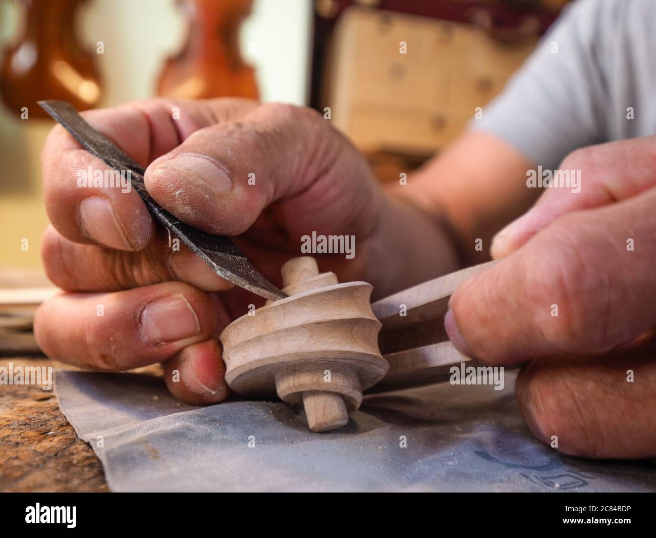 Hands of luthier violin maker carving and working on a instrument scroll in his workshop in Cremona, Italy Stock Photo