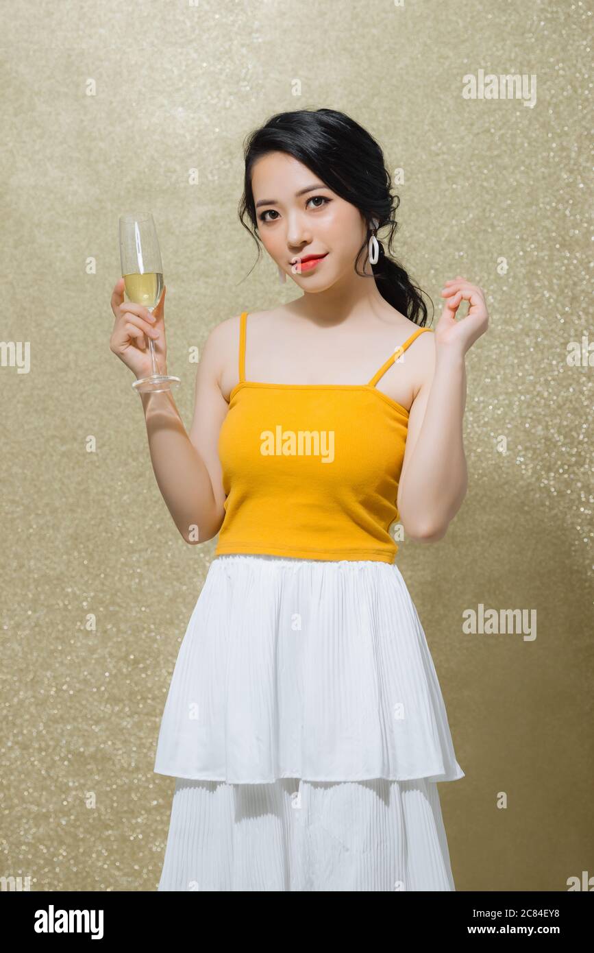 Portrait of beautiful young Asian woman holding wine glass over gold ...