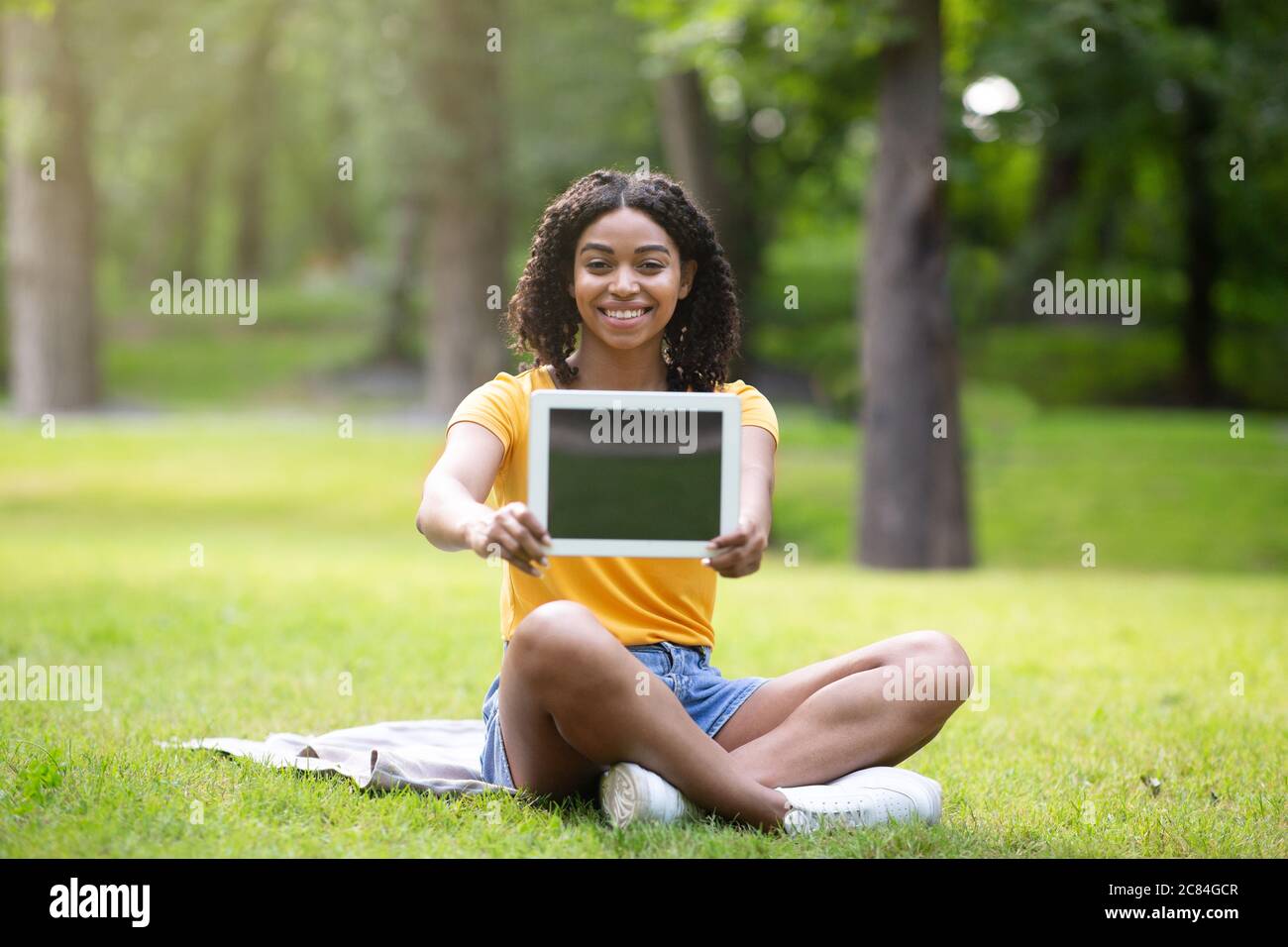 Happy African American girl showing tablet computer with empty screen ...