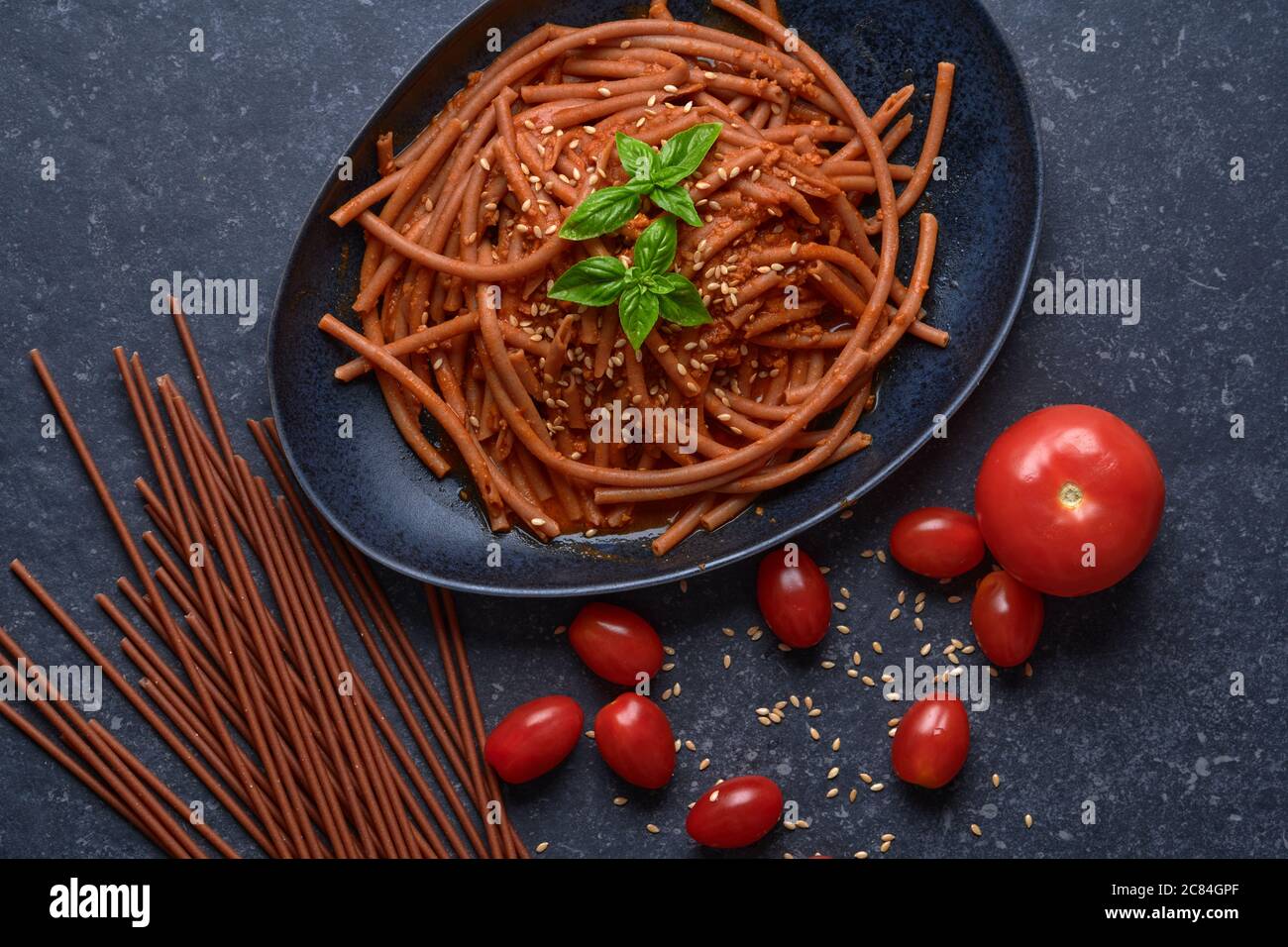 Bolognese vegan Bucatini, meatless, with soy sauce, tomatoes, sesame seeds and fresh basil, in black stone plate on dark background. Stock Photo