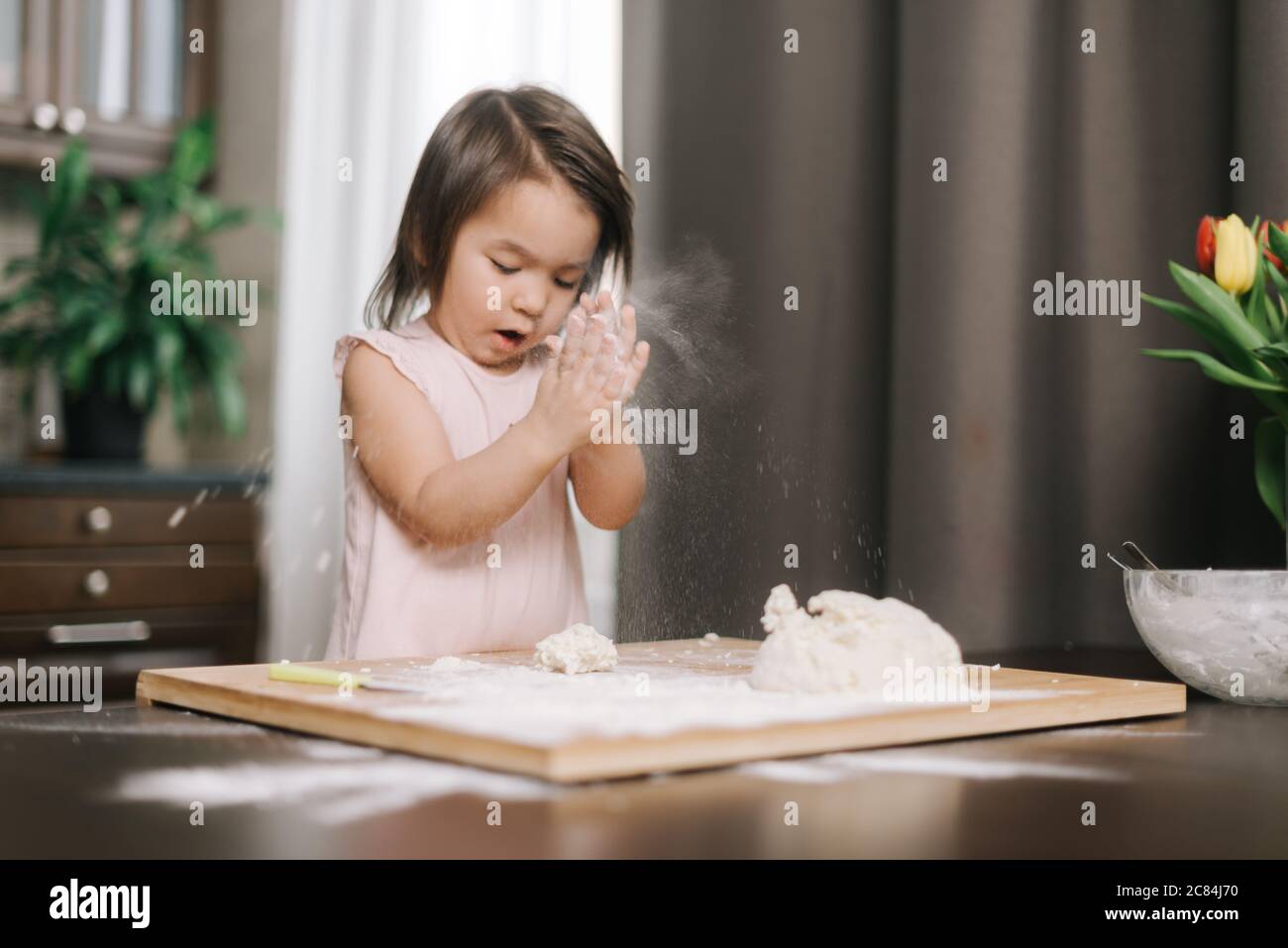 Beautiful little girl is clapping hands with flour. Child is playing