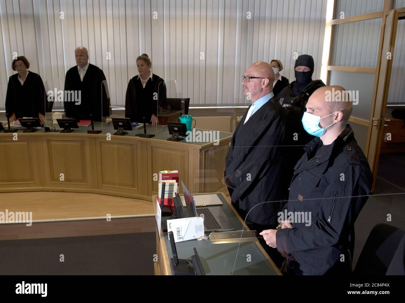 Magdeburg, Germany. 21st July, 2020. The accused Stephan Balliet (r) is standing next to his defence lawyer Hans-Dieter Weber (3rd from right) in the Regional Court at the beginning of the trial. In the background is the presiding judge Ursula Mertens (l). The Federal Prosecutor's Office accuses the assassin of Hall 13 of criminal offences, including murder and attempted murder. On 9 October 2019, on the highest Jewish holiday Yom Kippur, he had attempted to cause a bloodbath in the synagogue in Halle. Credit: Hendrik Schmidt/dpa-Zentralbild/Pool/dpa/Alamy Live News Stock Photo