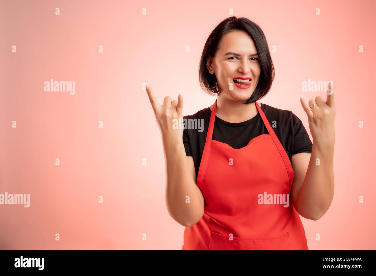 Woman employed at supermarket with red apron and black t-shirt, doing rock  symbol with hands up isolated on red background Stock Photo - Alamy