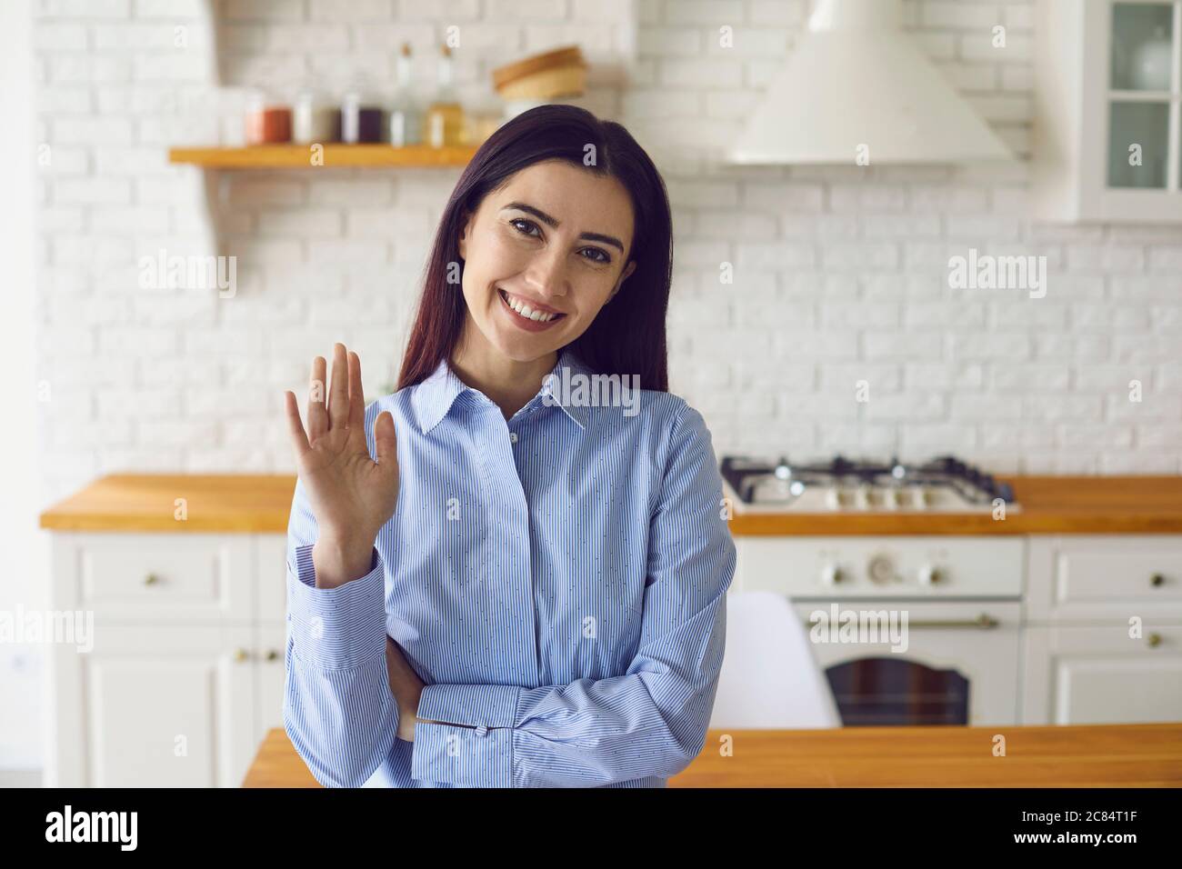 Content woman saying hello while standing in modern kitchen Stock Photo