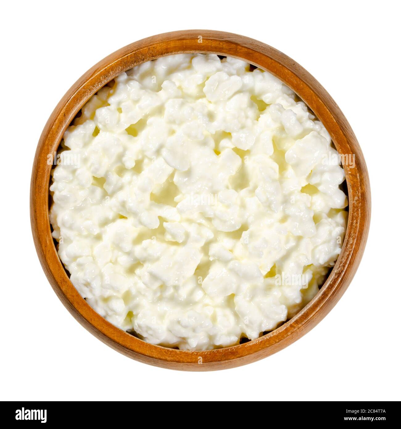Cottage cheese in wooden bowl. Fresh cheese curd product also known as curds and whey,  with mild flavor. A cream is added to the curd grains. Stock Photo