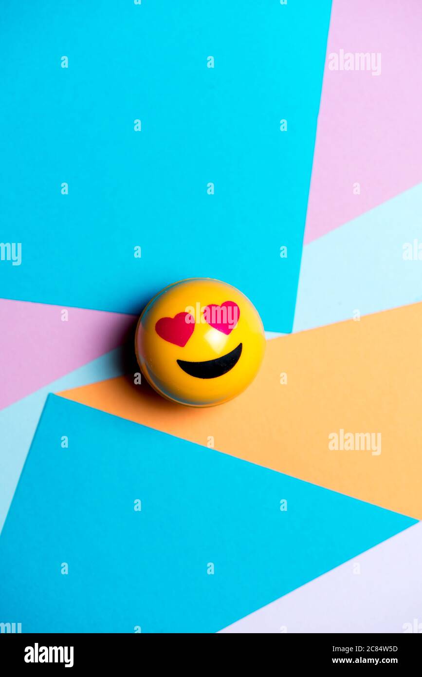 smiling yellow emoticon with heart eyes, on multicolored geometric texture, social media concept Stock Photo