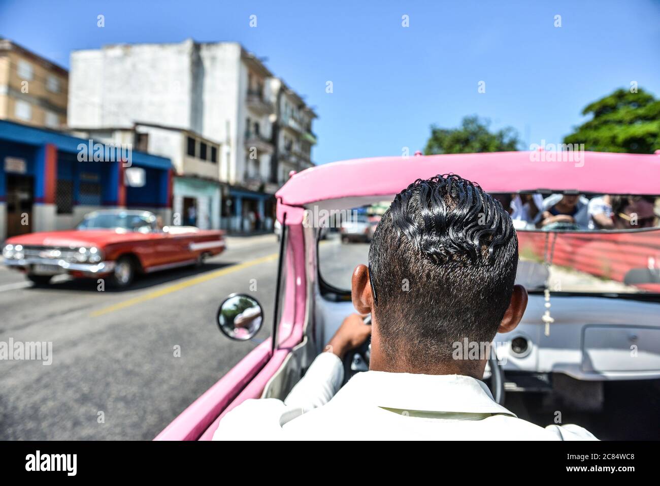Cuba, Havana: classic American cars. Two vehicles passing each other, including an old red Chevrolet. Man viewed from behind driving a taxi, a pink an Stock Photo