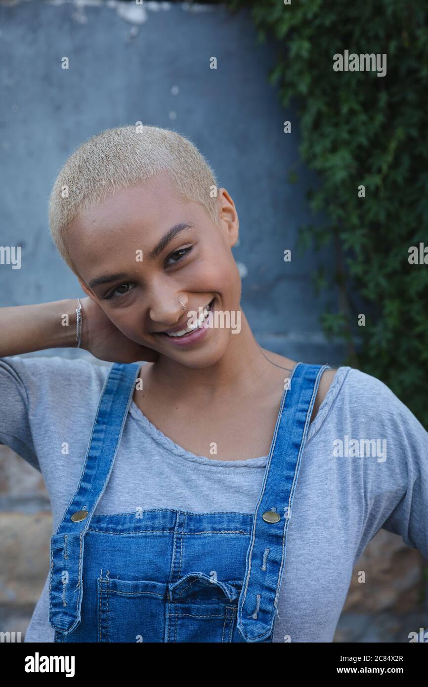 Portrait of mixed race alternative woman with short blonde hair wearing  denim dungarees, out and about in the city on a sunny day, looking to  camera a Stock Photo - Alamy