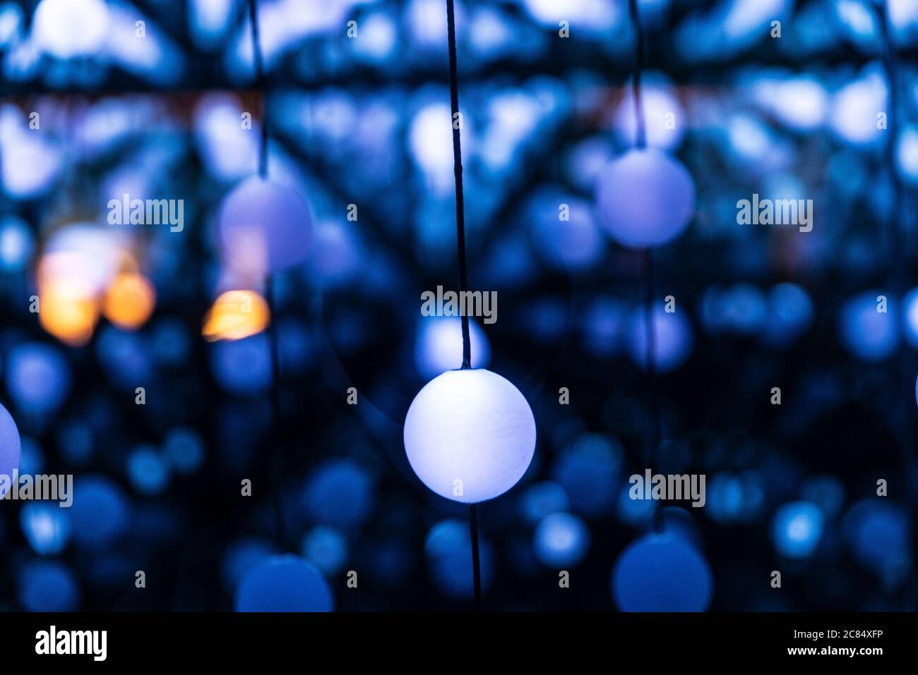 Many illuminated balls hung and linked by threads creating an infinite perspective as abstract blue background Stock Photo