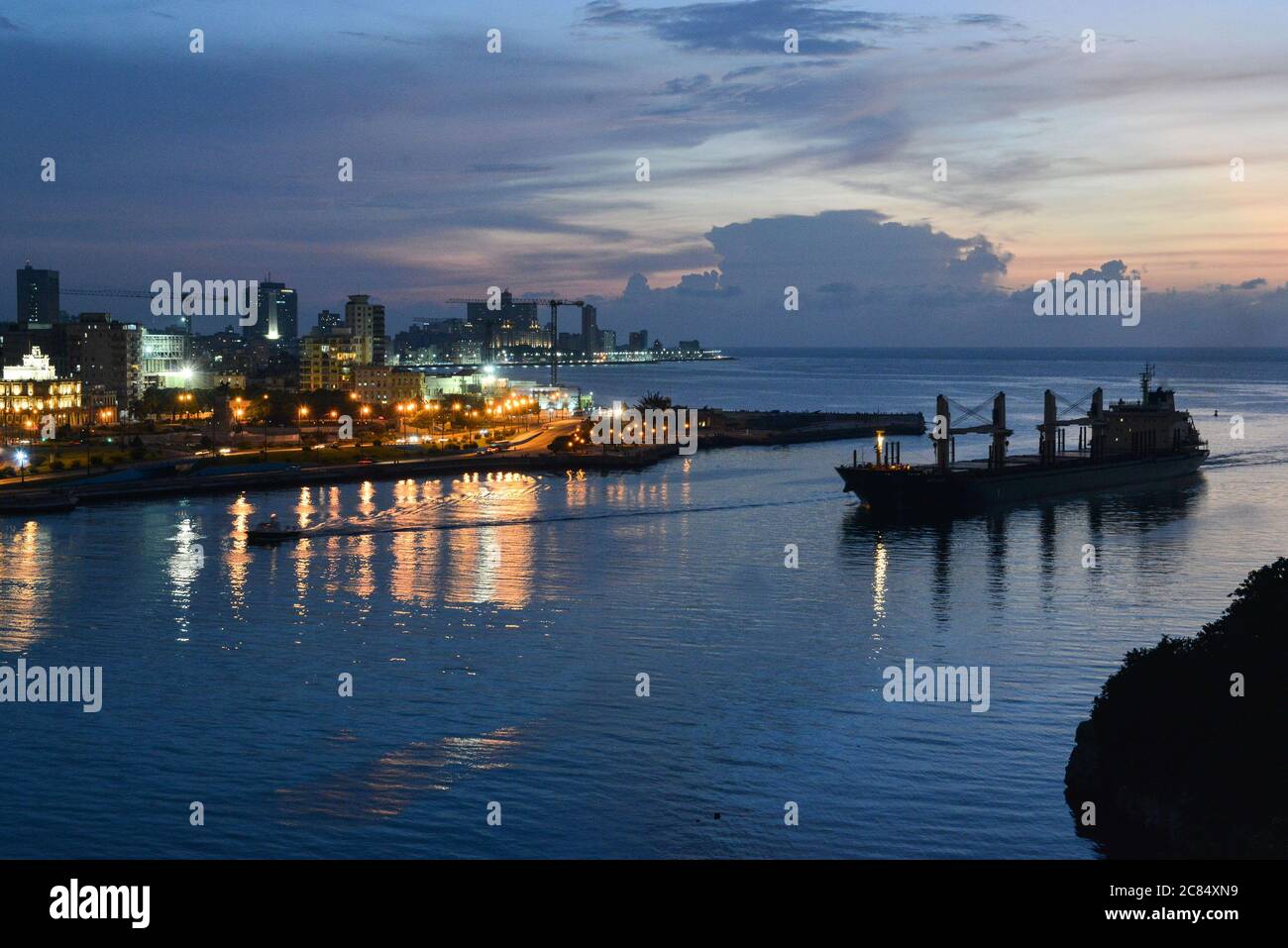 Cuba, Havana: night view of the illuminated quays of the city from the the Morro Castle. Cargo ship entering the bay Stock Photo