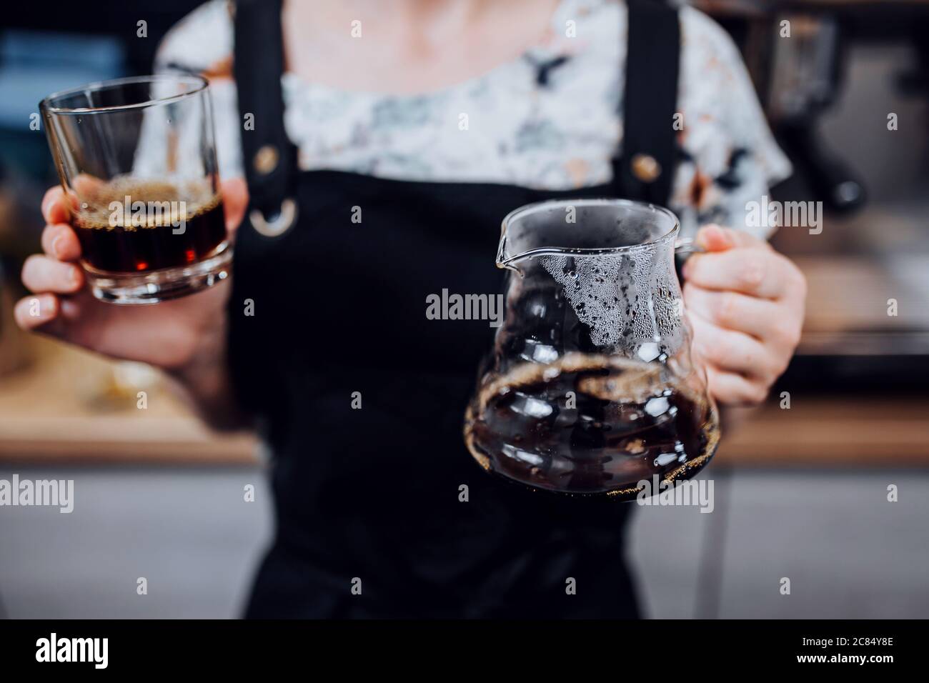 A glass of coffee prepared by a drip method in the female hands of a barista Stock Photo