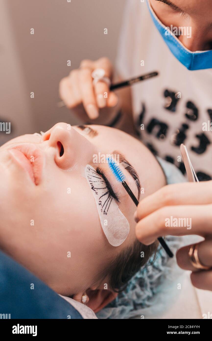 Professional qualified extension for a young girl - the master glues artificial eyelashes in bunches Stock Photo