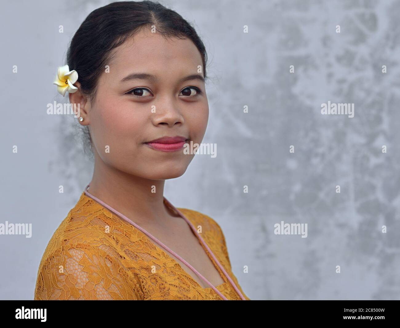 Young Balinese woman wears a Frangipani (Plumeria) flower in her hair and poses for the camera. Stock Photo