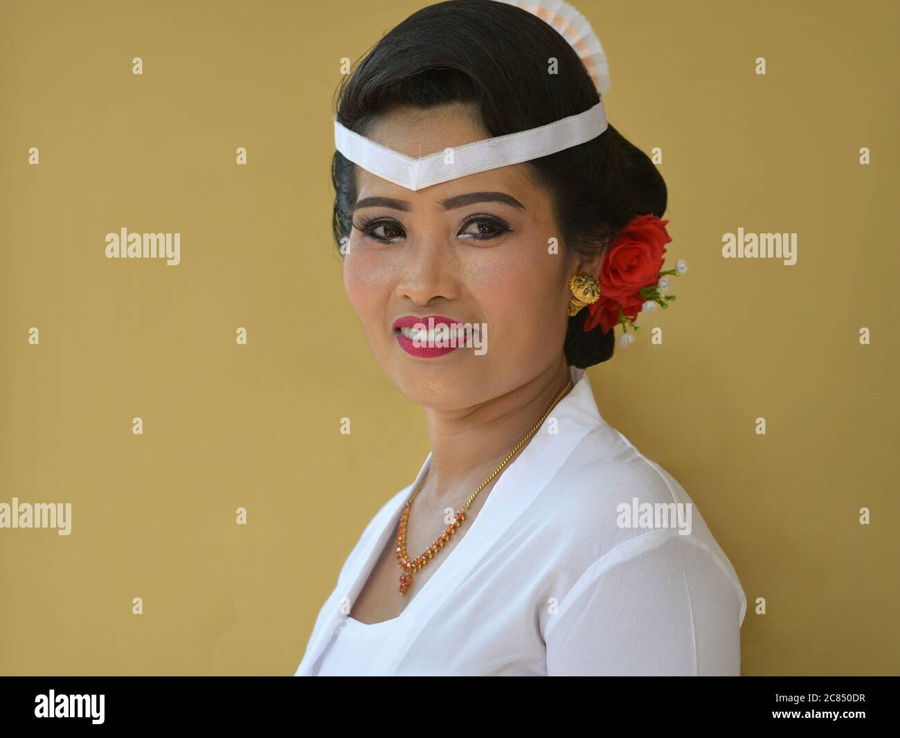 Indonesian Balinese woman wears white outfit and smiles for the camera during a religious Hindu temple ceremony (Odalan festival). Stock Photo