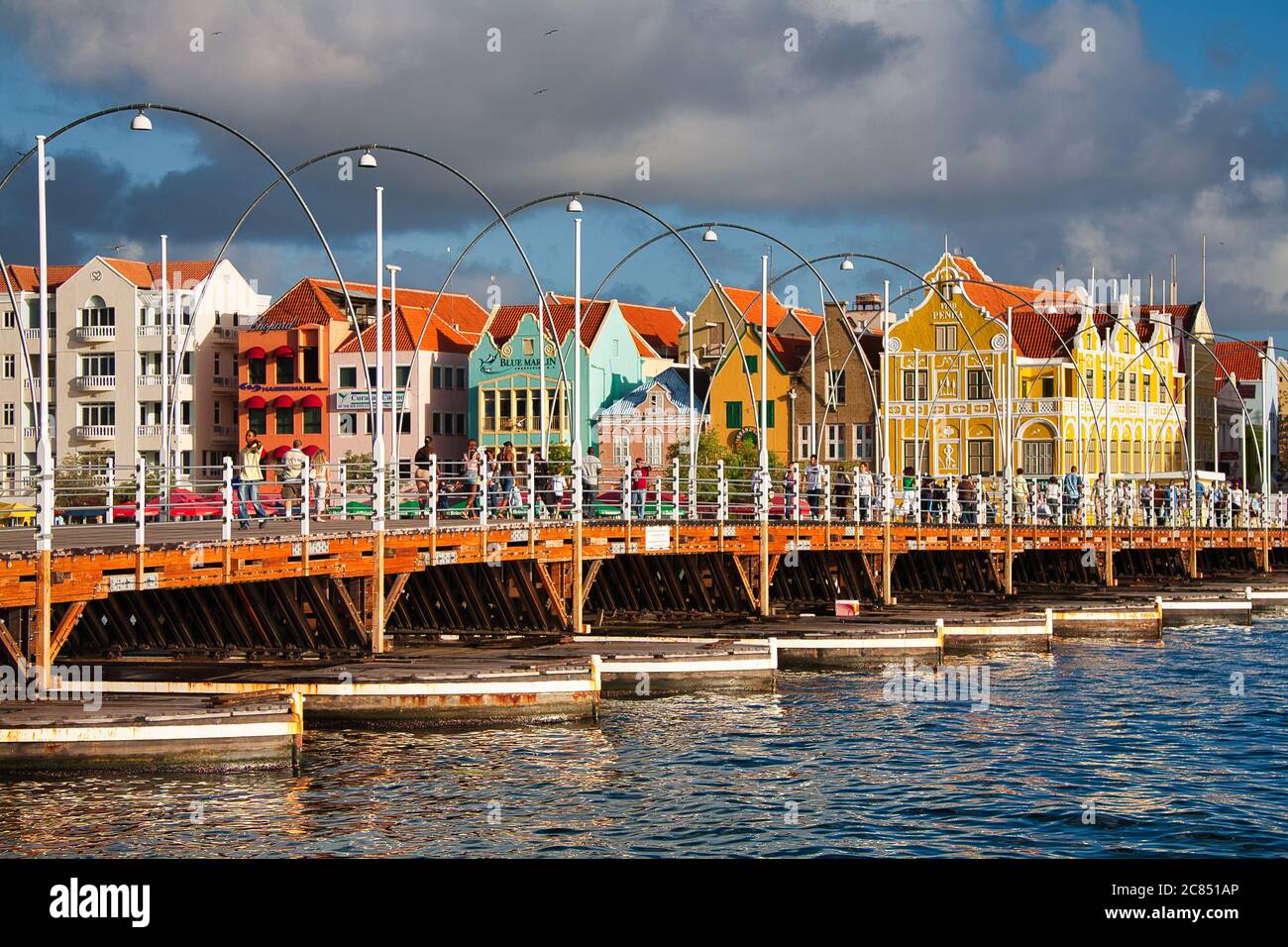 People walking over Queen Emma Bridge with typical Dutch style buildings in the background, Willemstat, Curacao, The Caribbean, West Indies Stock Photo