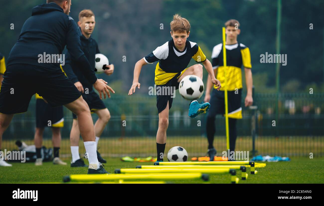 Teenage boys on football training session with two young coaches. Junior level soccer player kicking ball during practice session. Soccer training dri Stock Photo