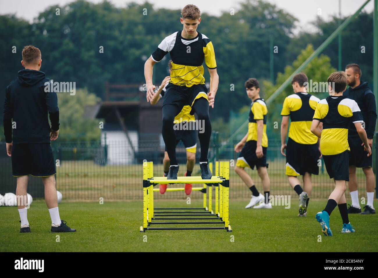 Soccer training drills with hurdles agility. Football players jumping high over hurdles obstacles. Footballers in a team on practice pitch. Two coache Stock Photo