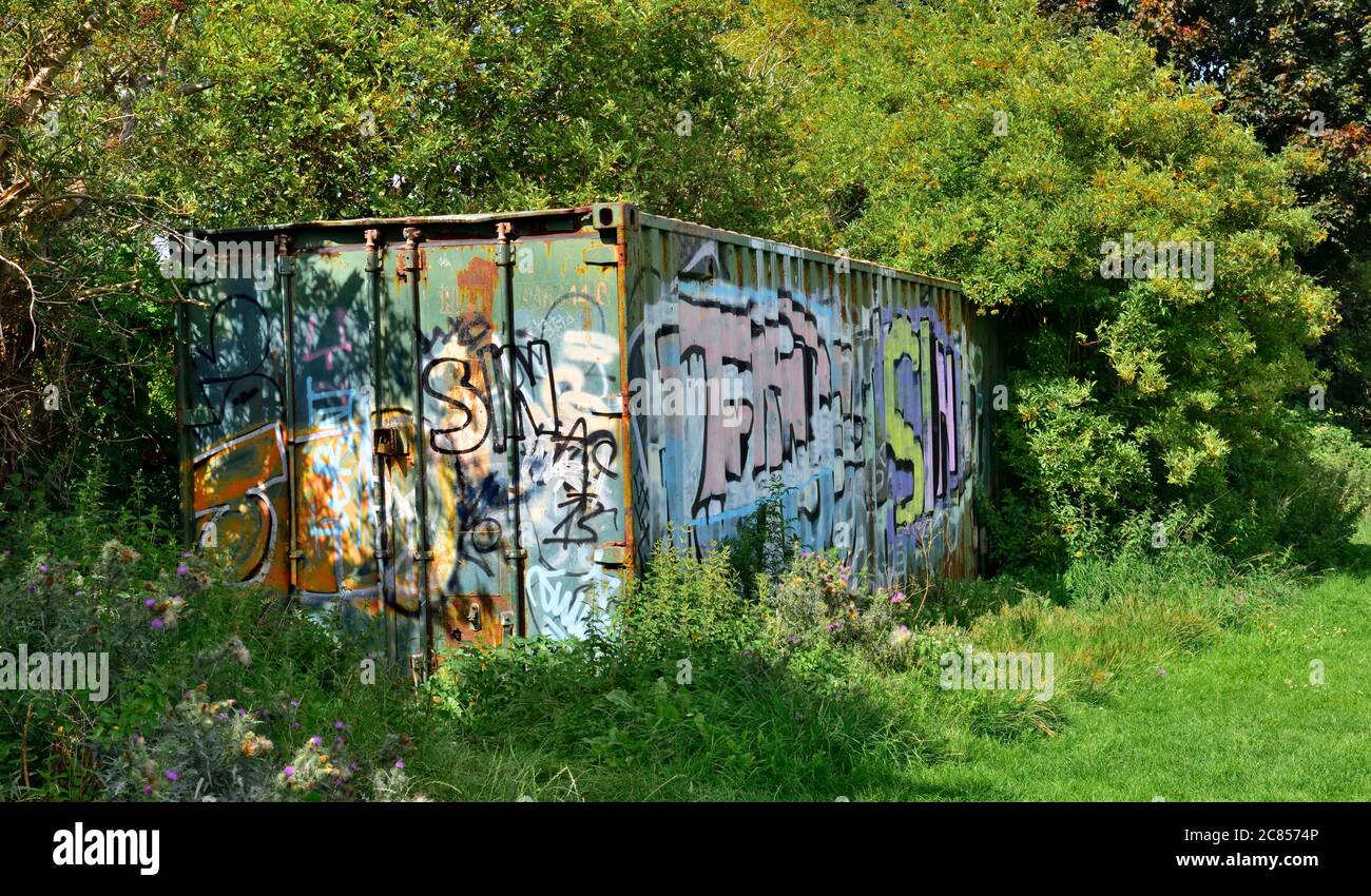 Derelict, abandoned overgrown shipping container used for storage covered in graffiti Stock Photo