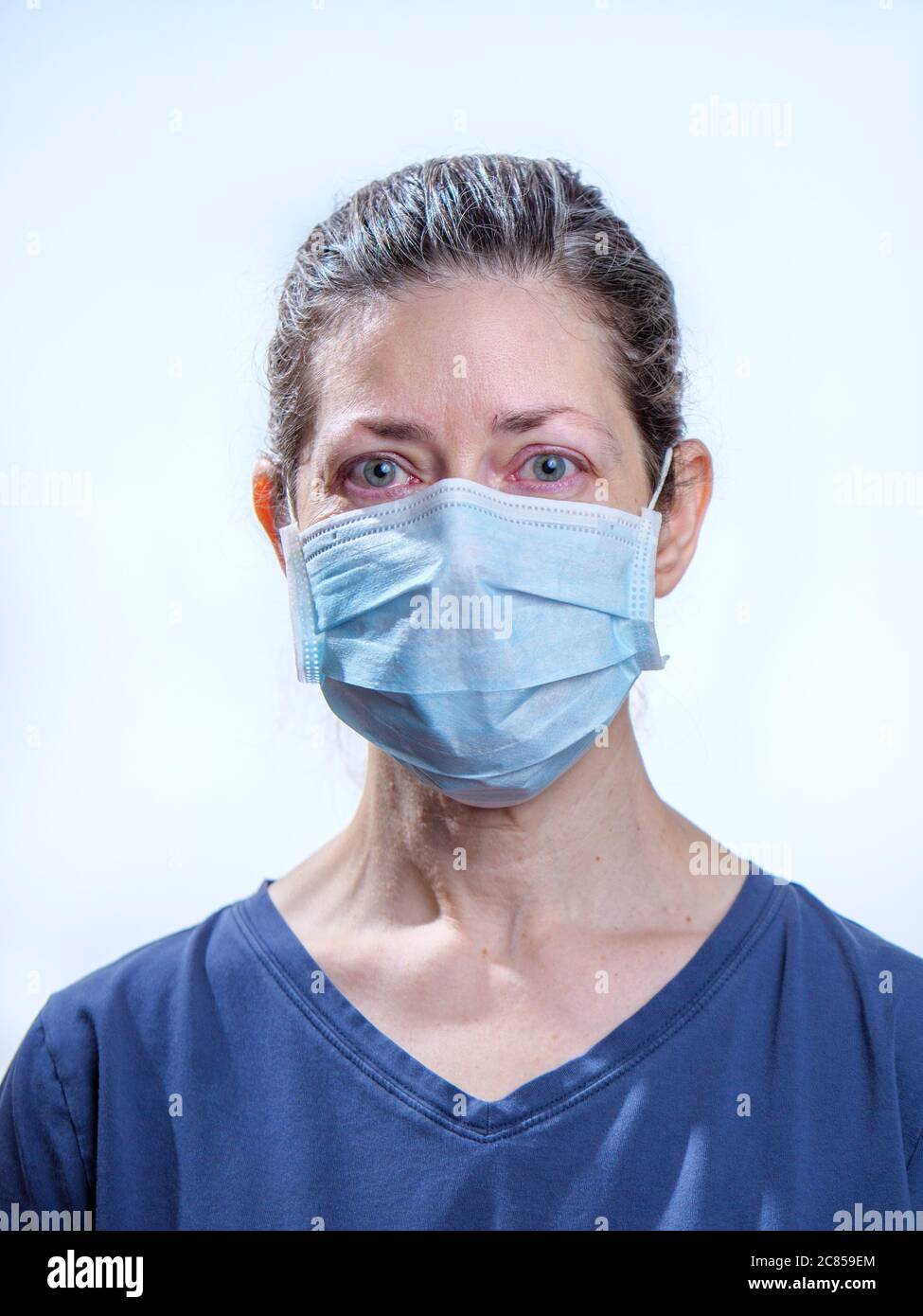 Female healthcare worker wearing surgical face mask, looking tired. Photo taken during COVID-19 pandemic. Model portrayal. Stock Photo