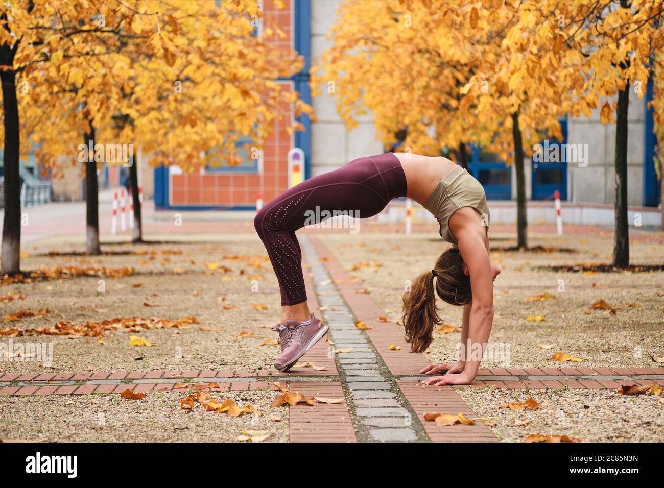 Young attractive sporty girl doing bridge exercise during yoga practice on autumn city street Stock Photo