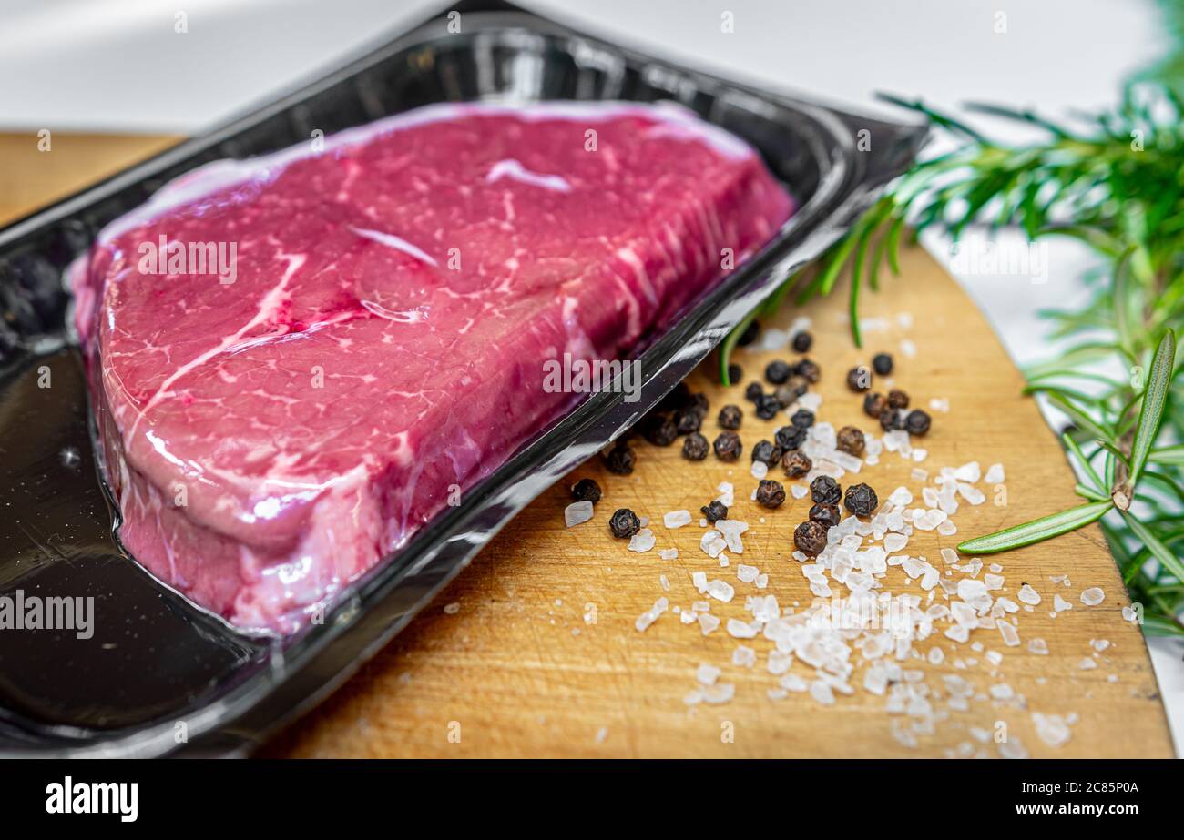 Vacuum-packed beef steak and spices on wooden chopping board Stock Photo