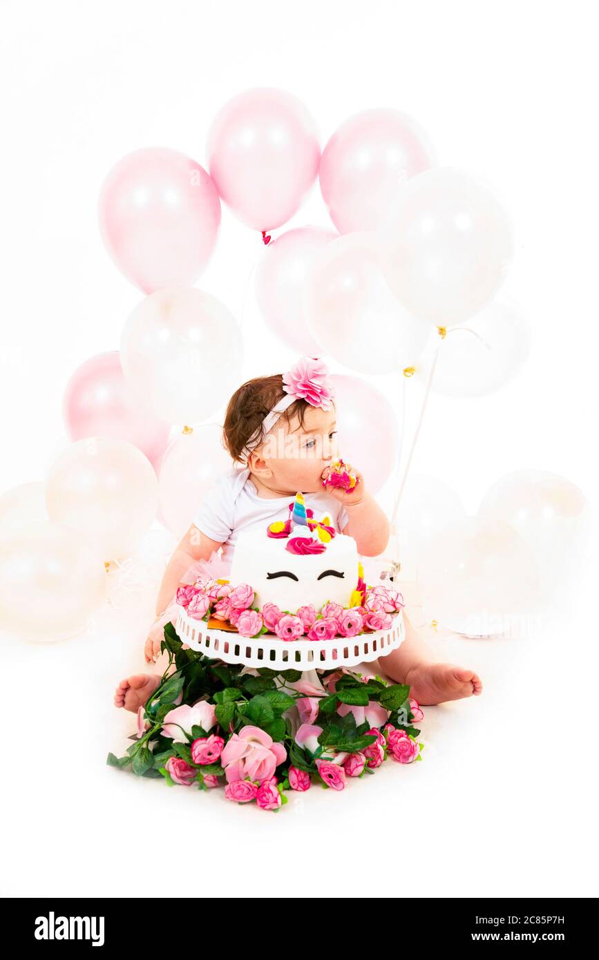 Vertical lifestyle portrait of a baby girl having a cake smash to celebrate her first birthday. Stock Photo