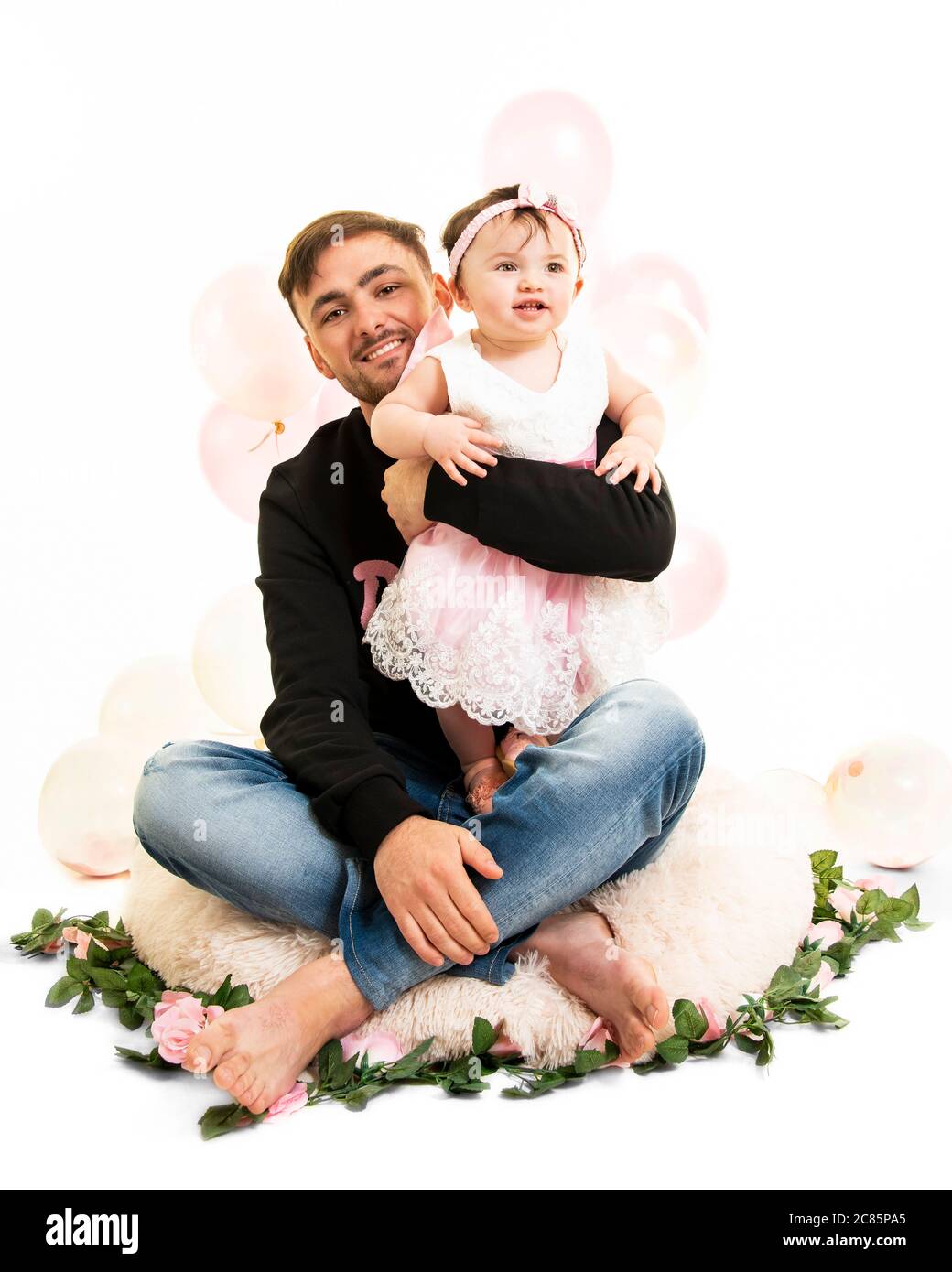Vertical lifestyle portrait of a young dad with his baby daughter on her first birthday. Stock Photo