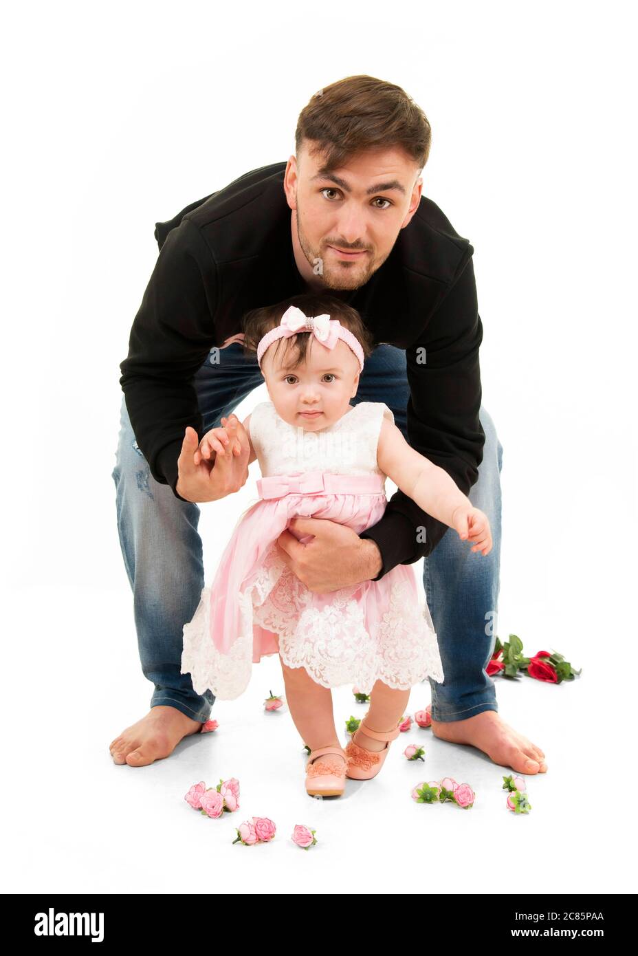 Vertical lifestyle portrait of a young dad helping his baby daughter to walk on her first birthday. Stock Photo