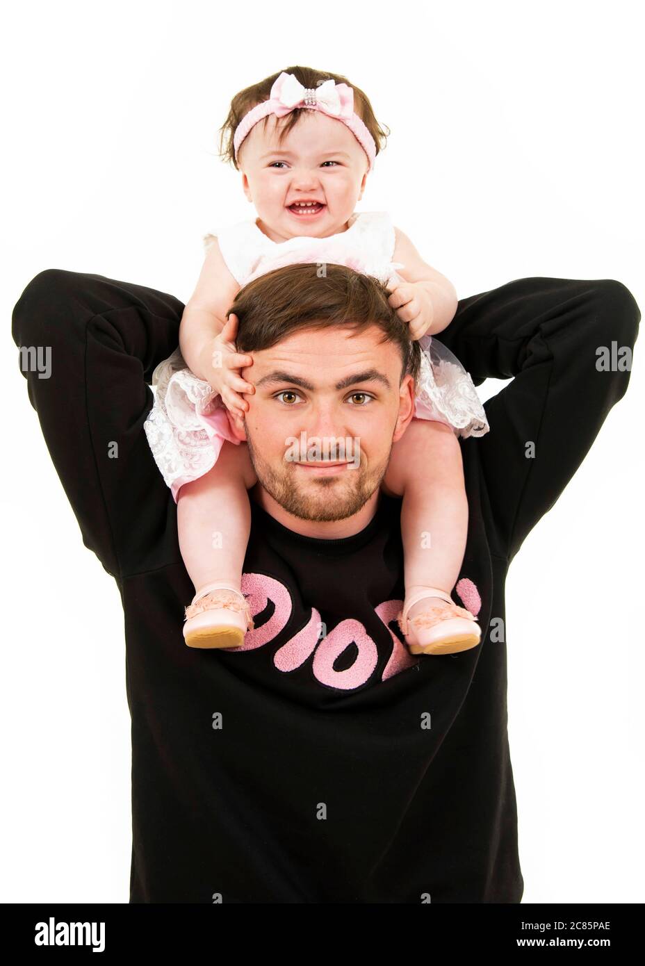 Vertical lifestyle portrait of a young dad with his baby daughter on his shoulders. Stock Photo