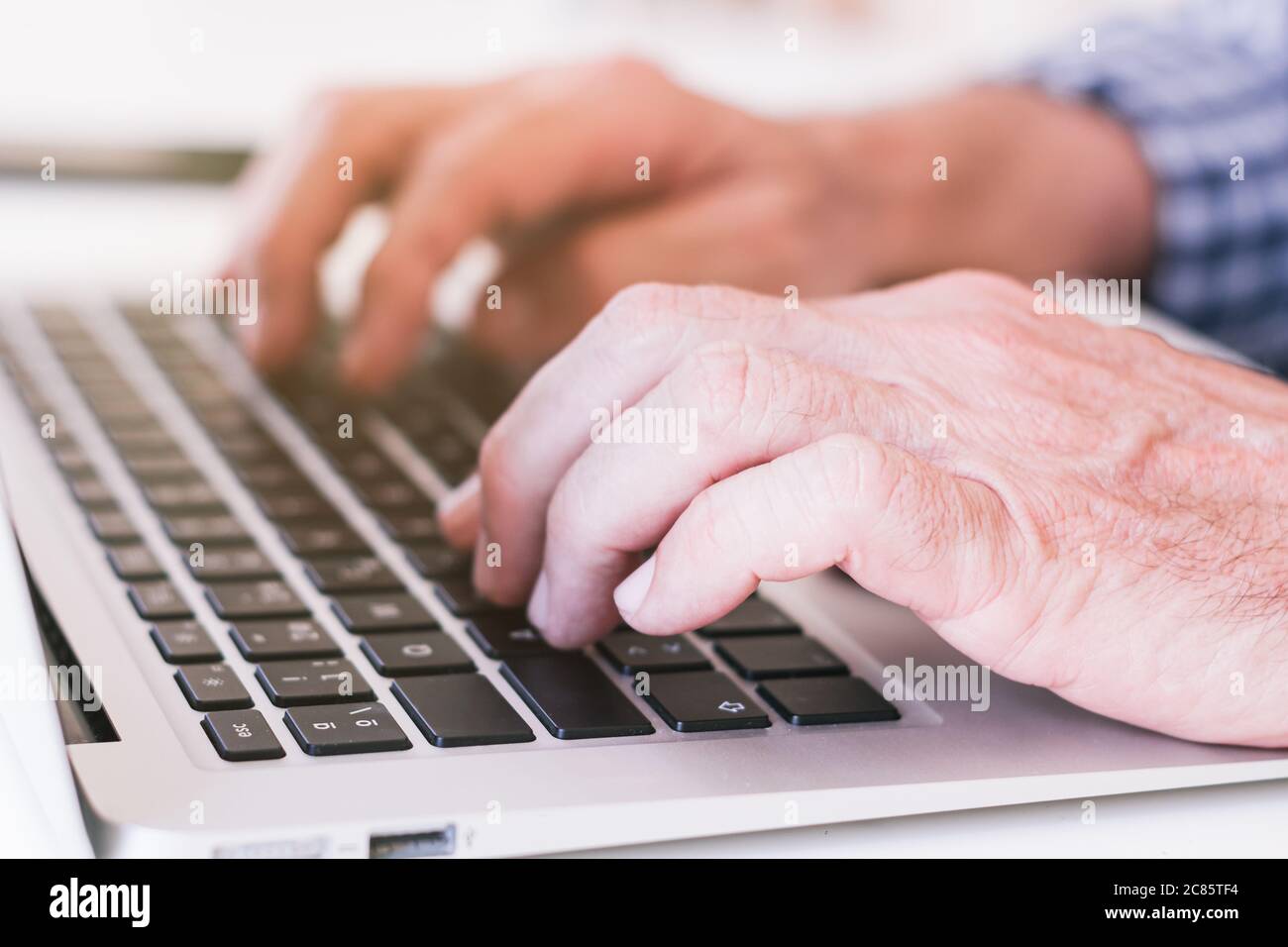 Older person's hands typing on a gray laptop. Selective focus. Stock Photo