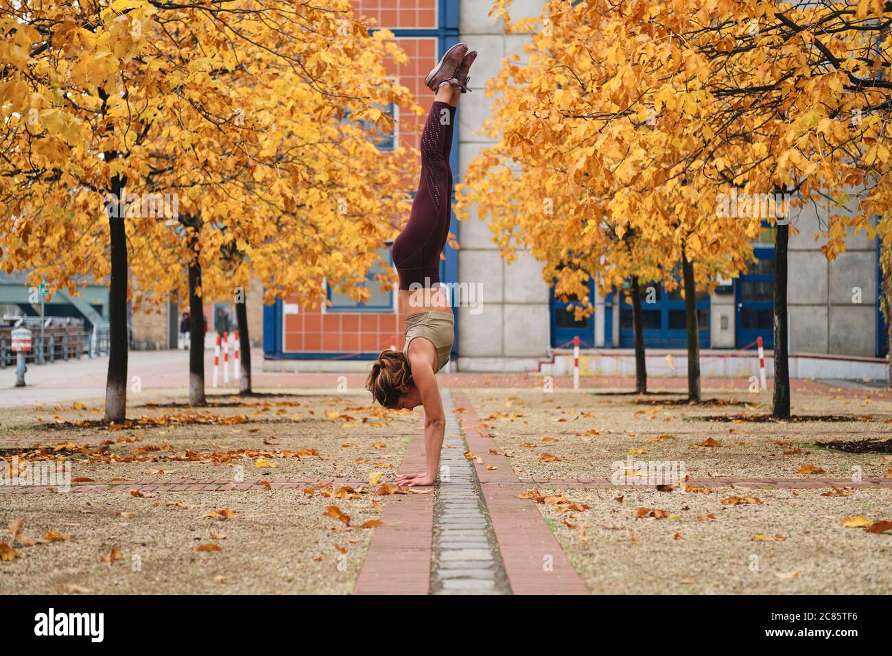 Beautiful strong sporty girl standing on hands during yoga practice on autumn city street Stock Photo