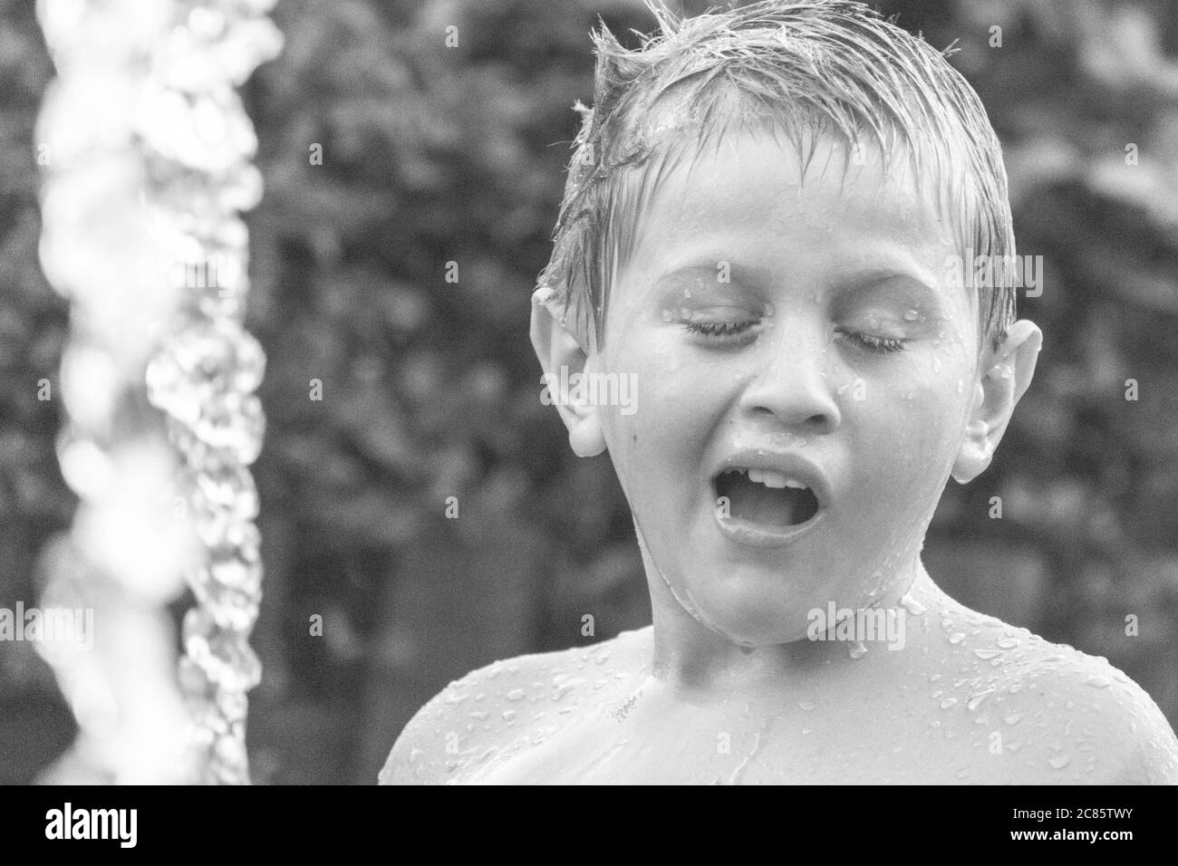 Beautiful grayscale shot of a young caucasian boy playing with water in a yard and having fun Stock Photo