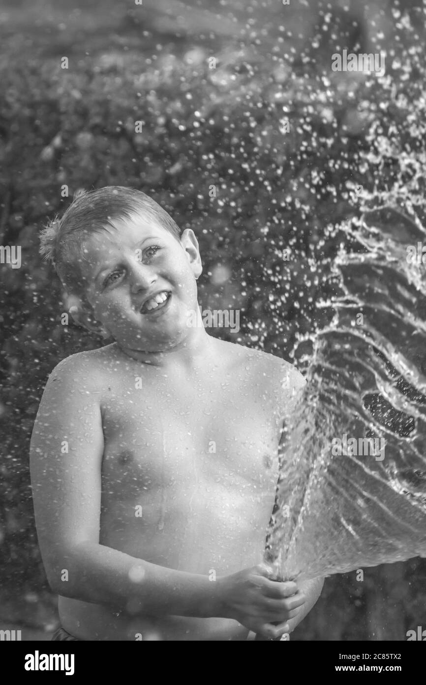 Beautiful grayscale shot of young caucasian boy playing with water in a yard and having fun Stock Photo