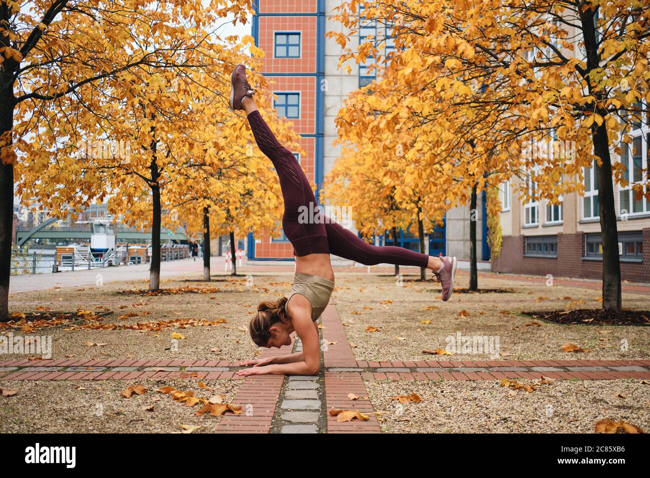 Beautiful girl in sportswear standing on hands during yoga practice on autumn city street Stock Photo