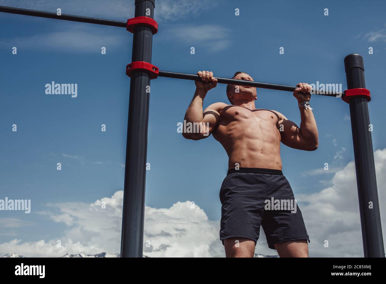 Caucasian male athlete with fit torso and strong hands doing chin ups ...
